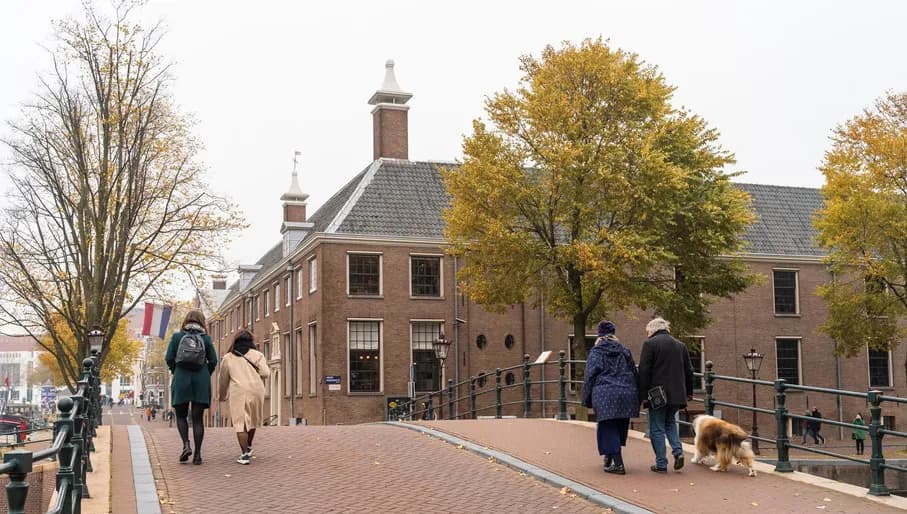 Singel street with museum De Hermitage at the right. A couple is crossing the bridge and another couple is walking their dog.