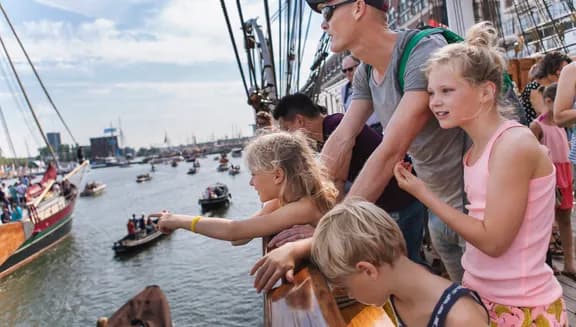 Bezoekers op de Christian Radich kijken naar de voorbijgaande bootjes.