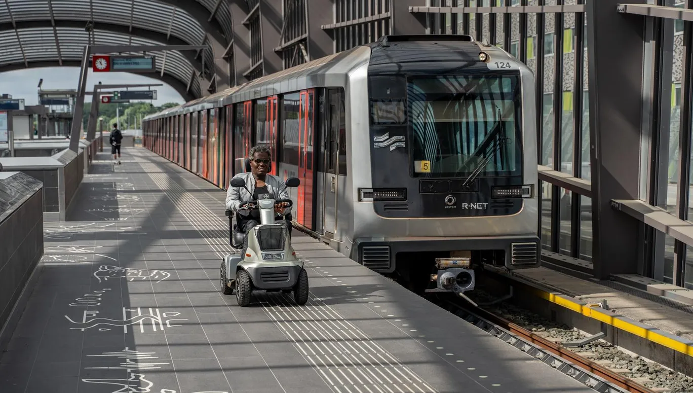 A person in an electric wheelchair riding on the metro platform.