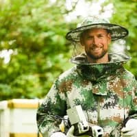 Cropped portrait of BeeSage founder Ru Wikmann wearing beekeeping outfit in pixelated camo colours.