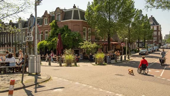 Cyclist and wheelchair user with dog crossing road towards restaurant terrace on Schinkelhavenstraat