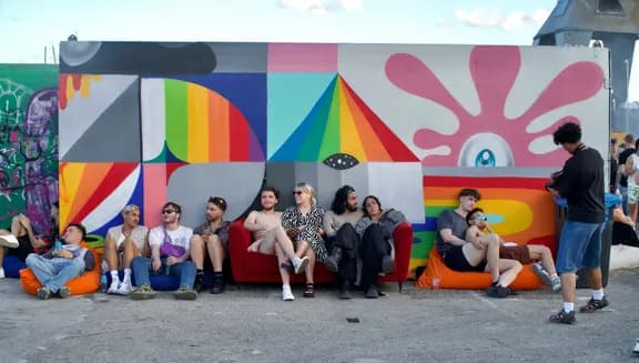 People lounging next a colourful wall at Tropikali Festival 2024.