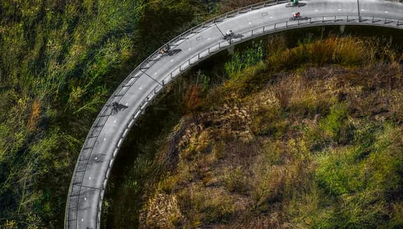 De gebogen hang-tuibrug en een van de langste fiets- en voetgangersbruggen van Nederland. De totale lengte van de brug is 780 meter en zorgt voor de verbinding tussen IJburg en de stad en overspant het Amsterdam-Rijnkanaal. De lange baan aan beide uiteinden zorgen voor een gemakkelijk ondiepe helling voor fietsers. De overspanning is sinds 2006 geopend voor voetgangers en fietsers. Het ontwerp van de oeververbinding werd vanwege zijn 'elegantie' in 2006 bekroond met de Nationale Staalprijs. Foto John Gundlach