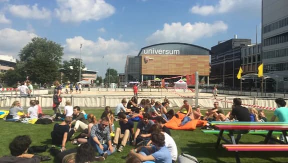 Students sitting on the grass in summer in front of University building of Physics UvA