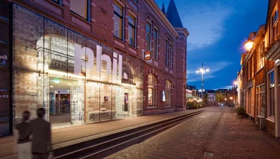 Couple walking past the exterior of PHIL Haarlem concert hall at night