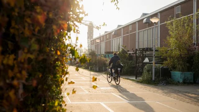 A parent cycling with his child over a sunny Scheepsbouwkade during early autumn.