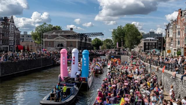 A crowd of people on the streets and in a boat with flags and signs - Pride Canal Parade