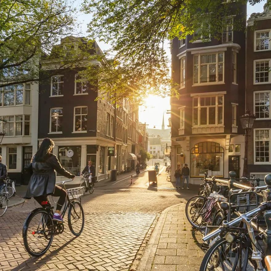 Amsterdam, Netherlands - September 22, 2021: Early morning in Amsterdam. Artistic image.  People ride bicycles, the ancient European city of Amsterdam. Sunlight and silhouettes, beautiful downtown houses.  Amsterdam, Holland, Netherlands, Europe