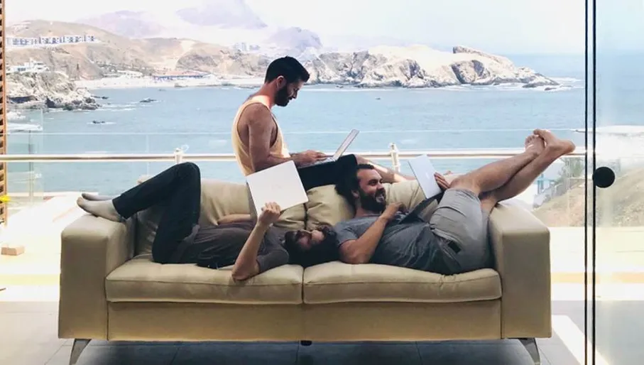 Three members of Settly product team sharing sofa with glass wall behind them showing dramatic coastal view.