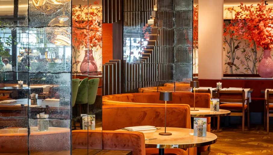 Dining area of Van der Valk hotel Schiphol, with circular booths, plants and a reflective wall.