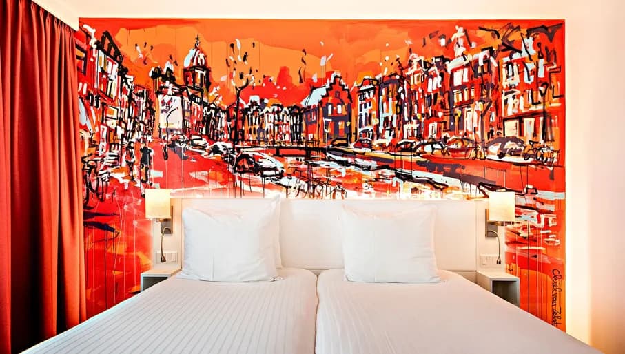 Interior of bedroom in Westcord Art Hotel, with impressionistic painting of Amsterdam canalhouses behind bed.