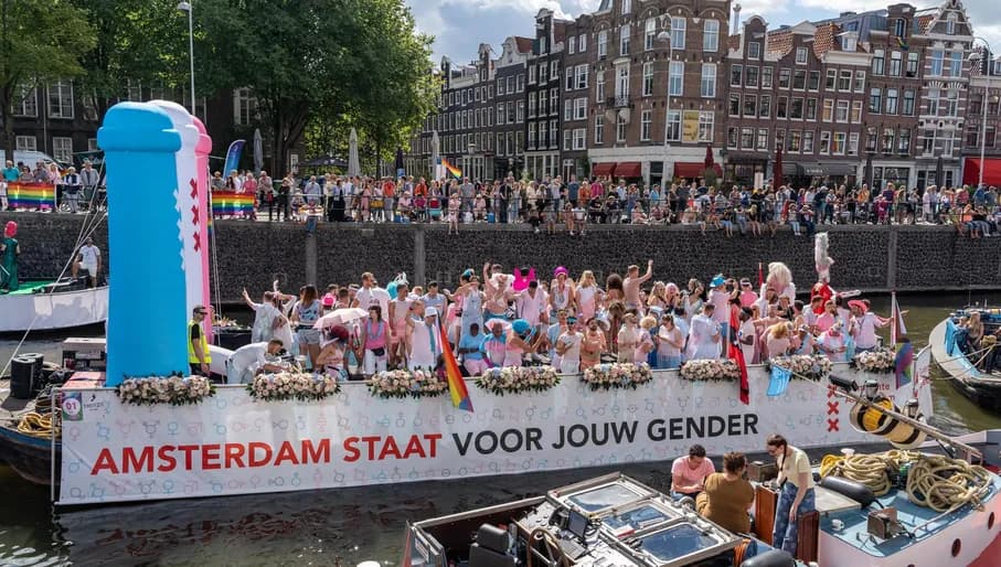 A crowd of people on the streets and in a boat with flags and signs - Pride Canal Parade