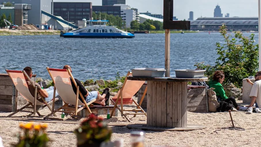 People lounging on beach chairs at Pllek with view over 't IJ