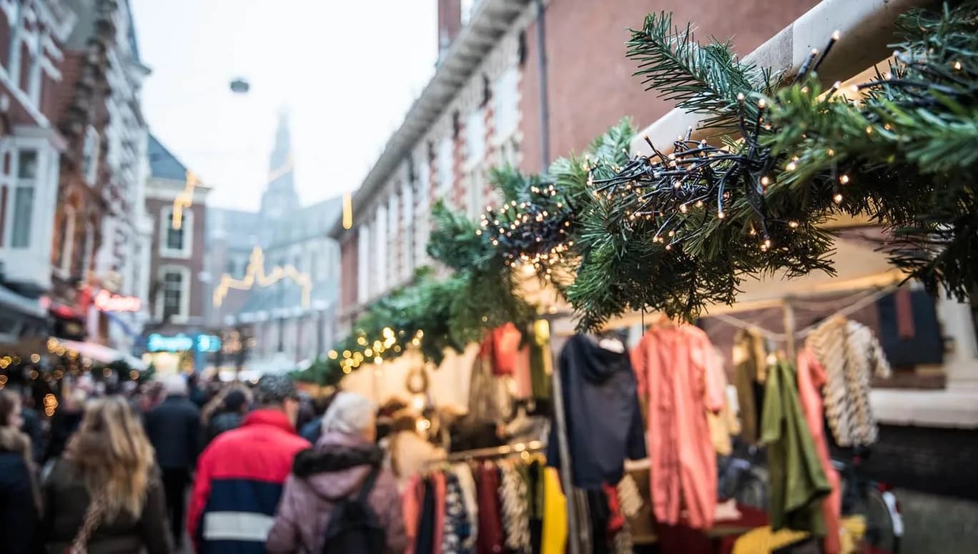 Christmas market in Haarlem. With a close-up of a pine branch covered in Christmas lights with a market and church tower in the background.