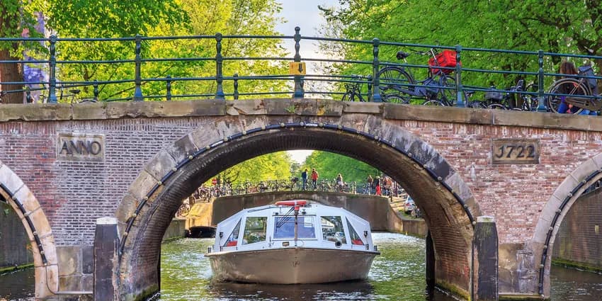 Canal cruise boat goes under the bridge over the Herengracht canal.