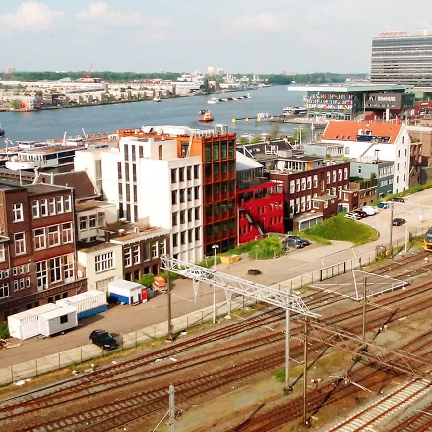 Train tracks in Amsterdam with IJ river visible behind buildings.